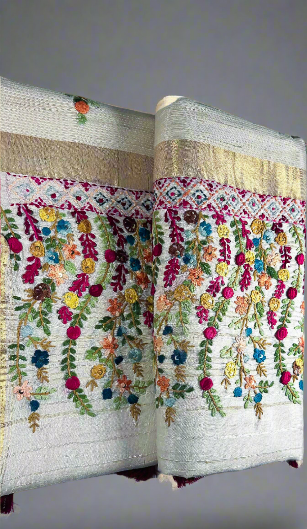 Off-white semi tussar silk saree with multicolor Resham thread embroidery, golden zari border, and maroon tassels.