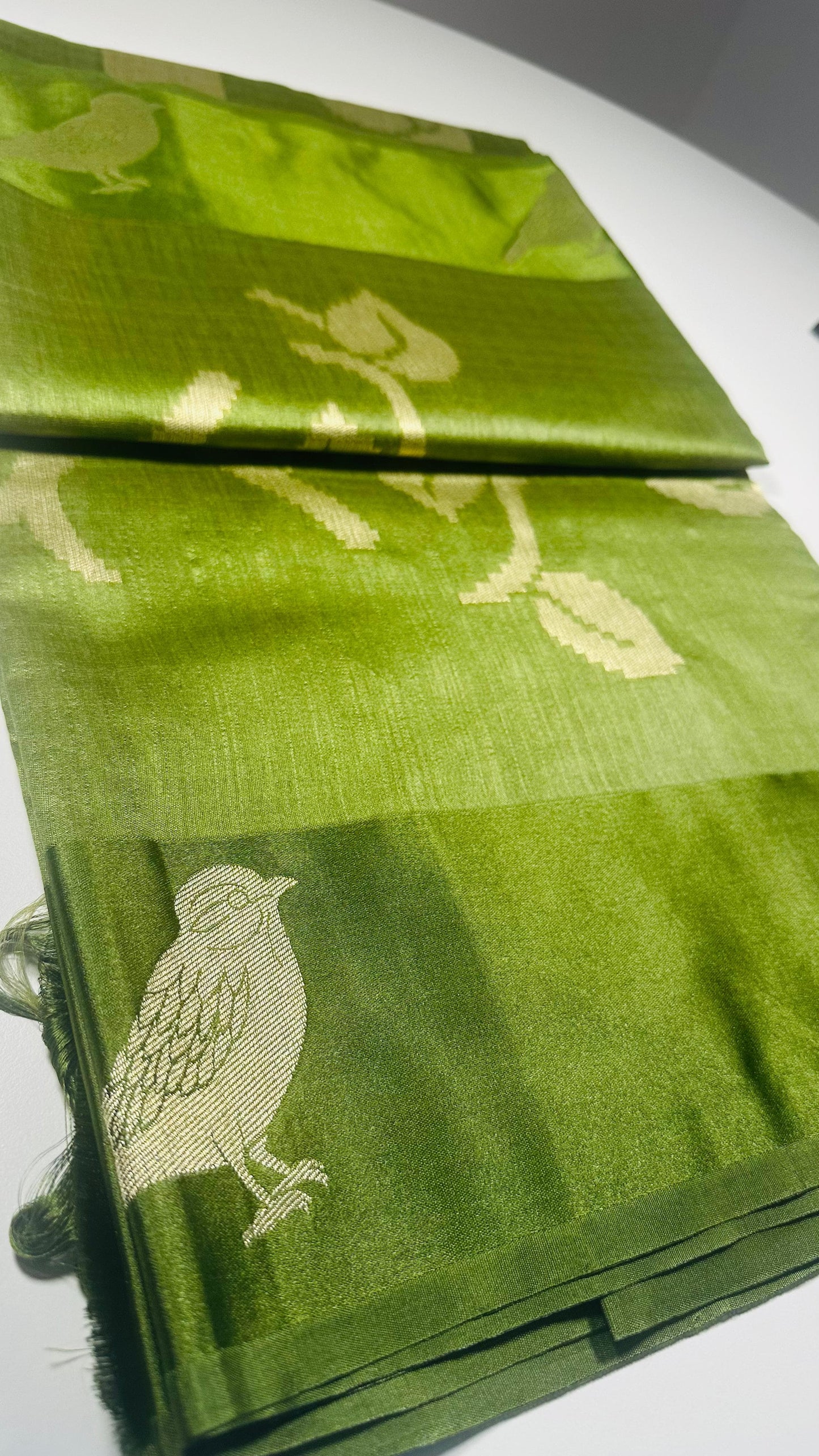 Green silk saree with woven bird and leaf motifs showing nature-inspired traditional Indian design and lustrous silk fabric