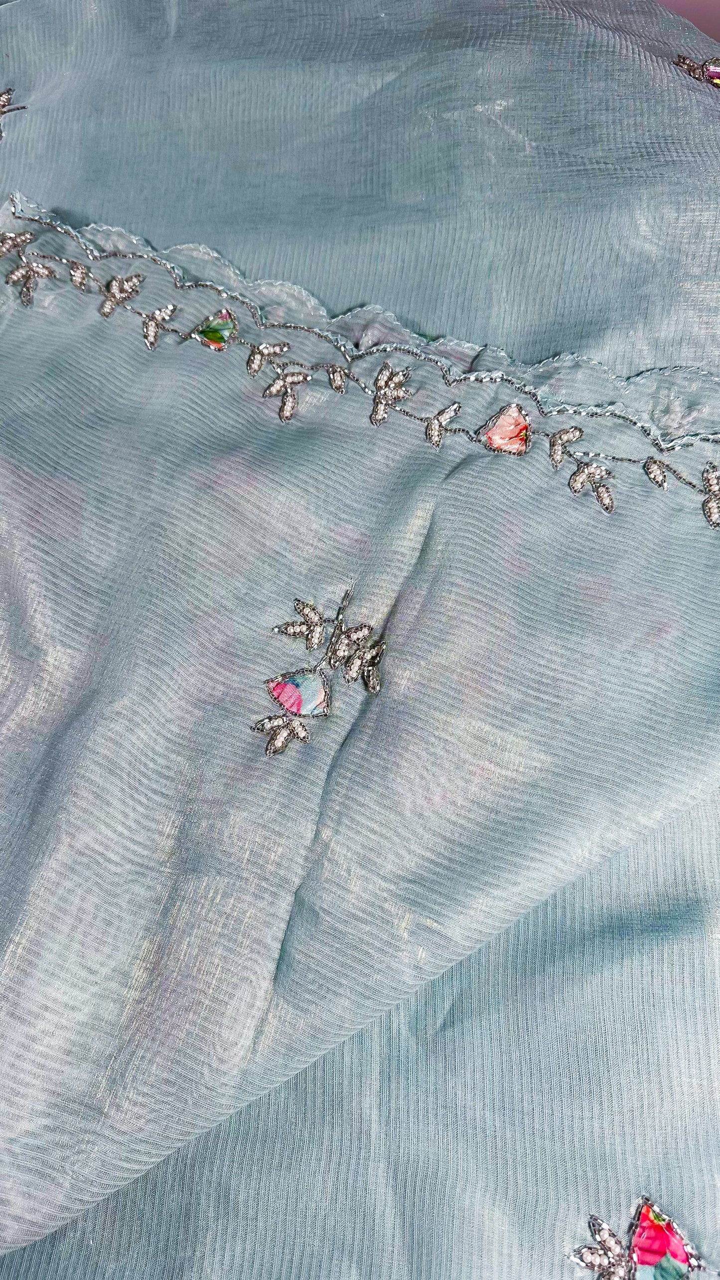 Close-up of embroidered floral motifs on powder blue saree with silver threadwork and coloured stone accents