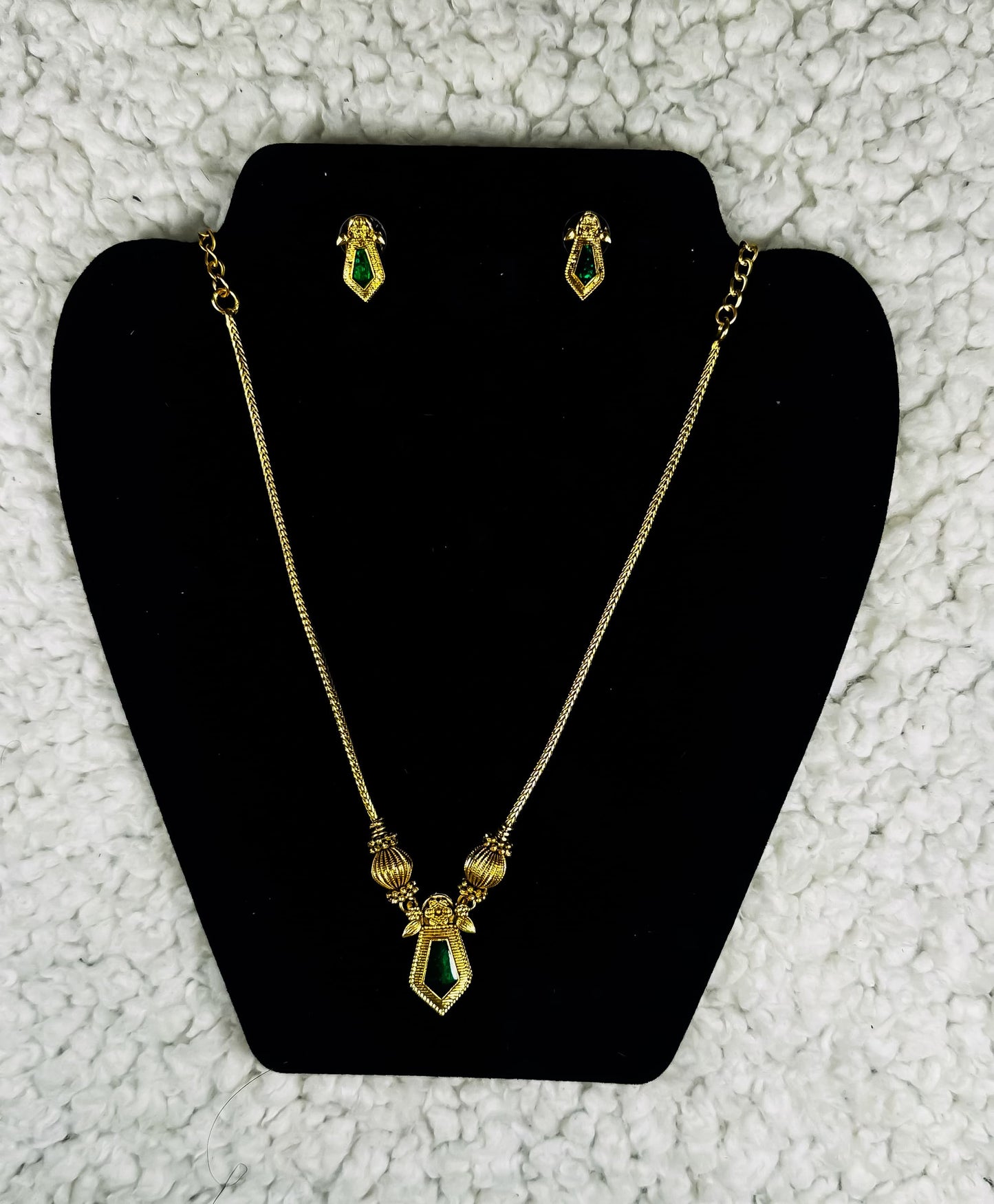 Gold plated geometric necklace and earrings jewelry set with emerald green diamond-shaped pendants displayed on black velvet jewelry stand