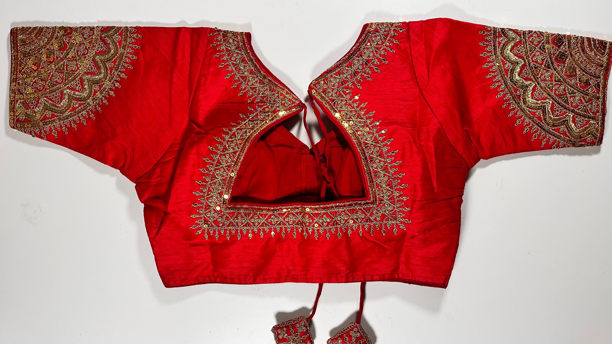 Back view of red silk blouse showing tie-up design with embroidered tassels and detailed traditional bridal embroidery work