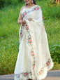 Woman wearing a white saree with floral embroidery standing in a grassy area.