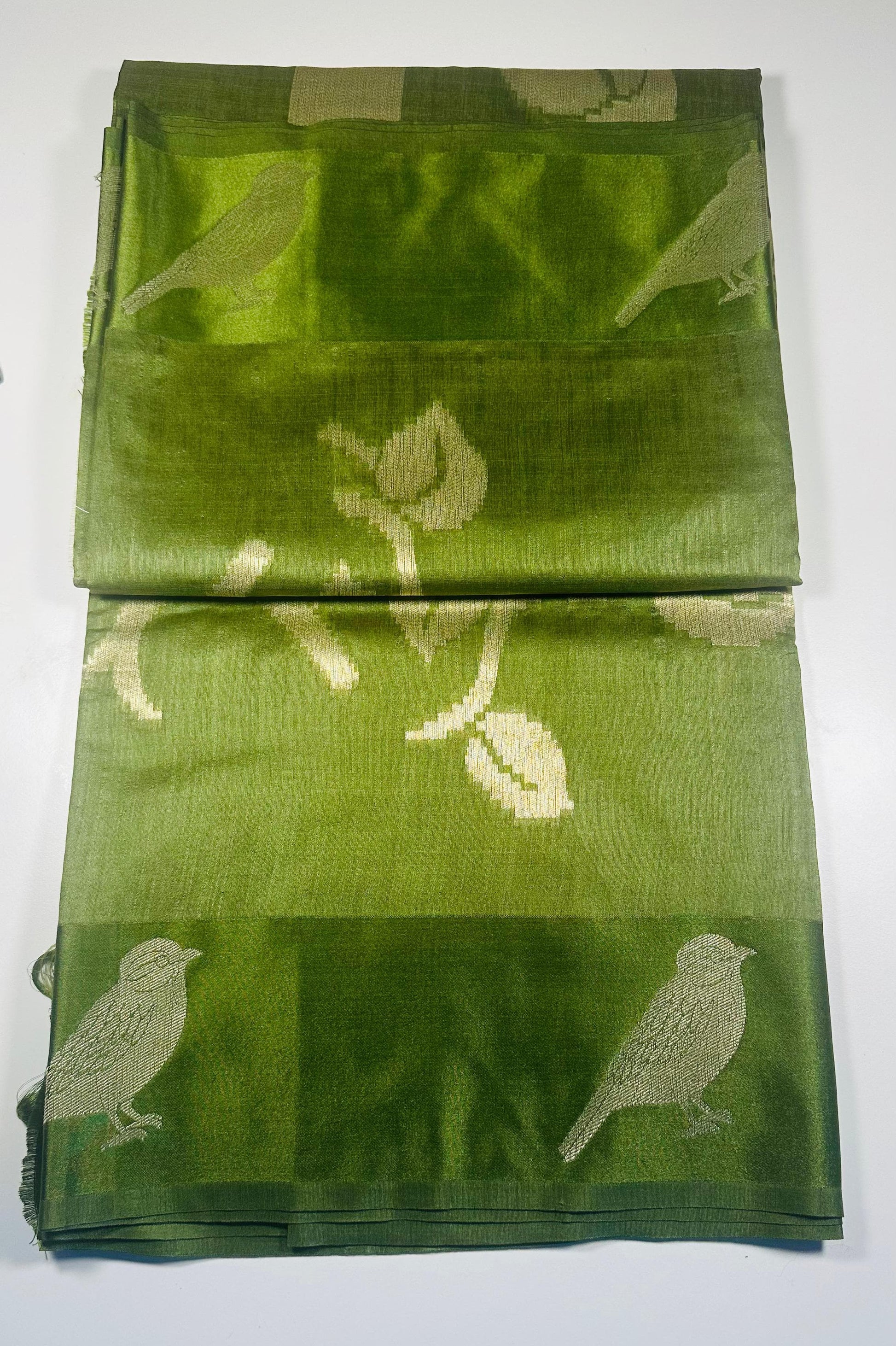 Green silk saree with woven bird and leaf motifs showing nature-inspired traditional Indian design and lustrous silk fabric