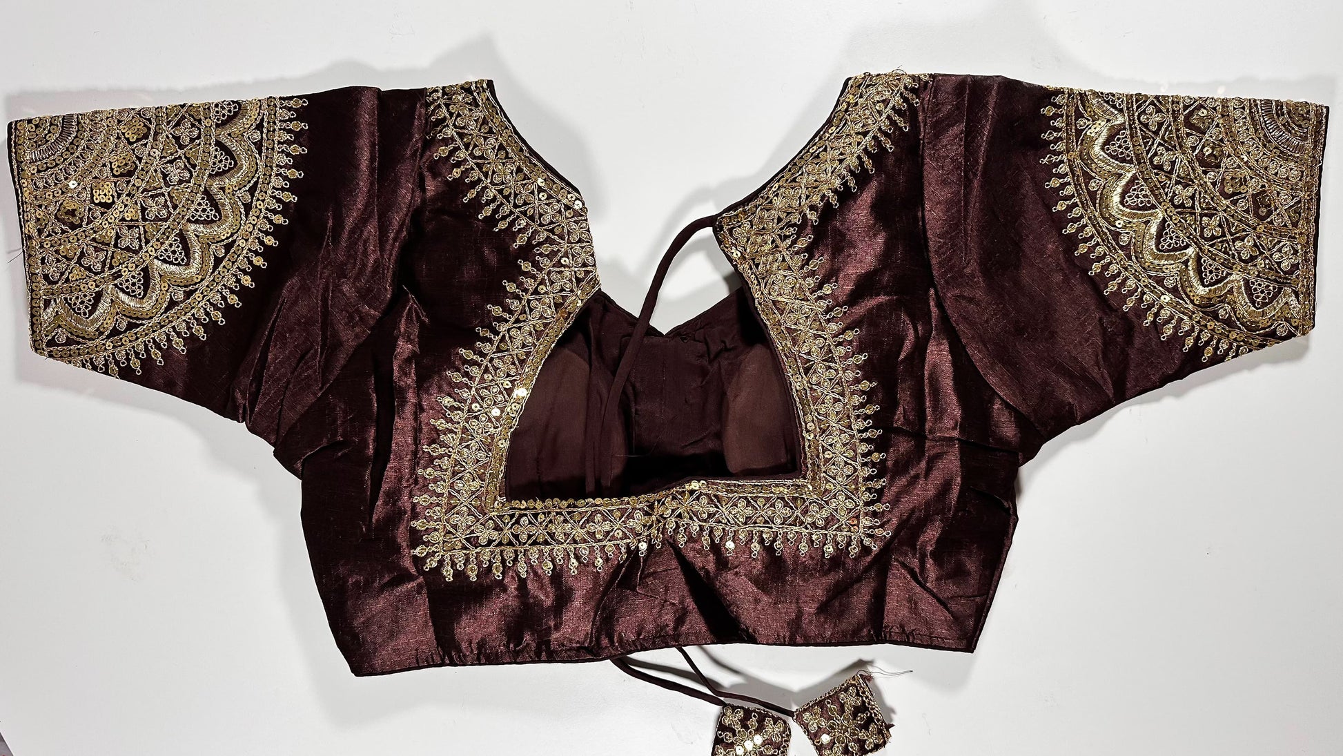 Back view of maroon silk blouse showing tie-up design with embroidered tassels and detailed traditional embroidery work