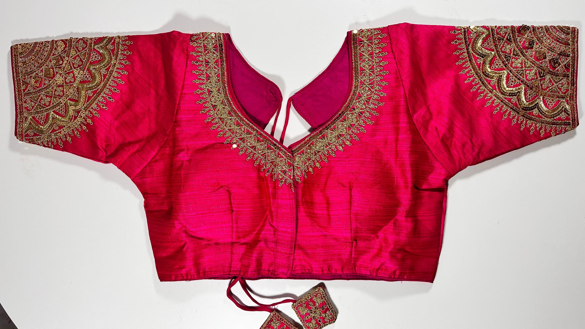 Bright pink embroidered saree blouse with heavy zardozi work showing traditional Indian bridal choli design with intricate gold handwork