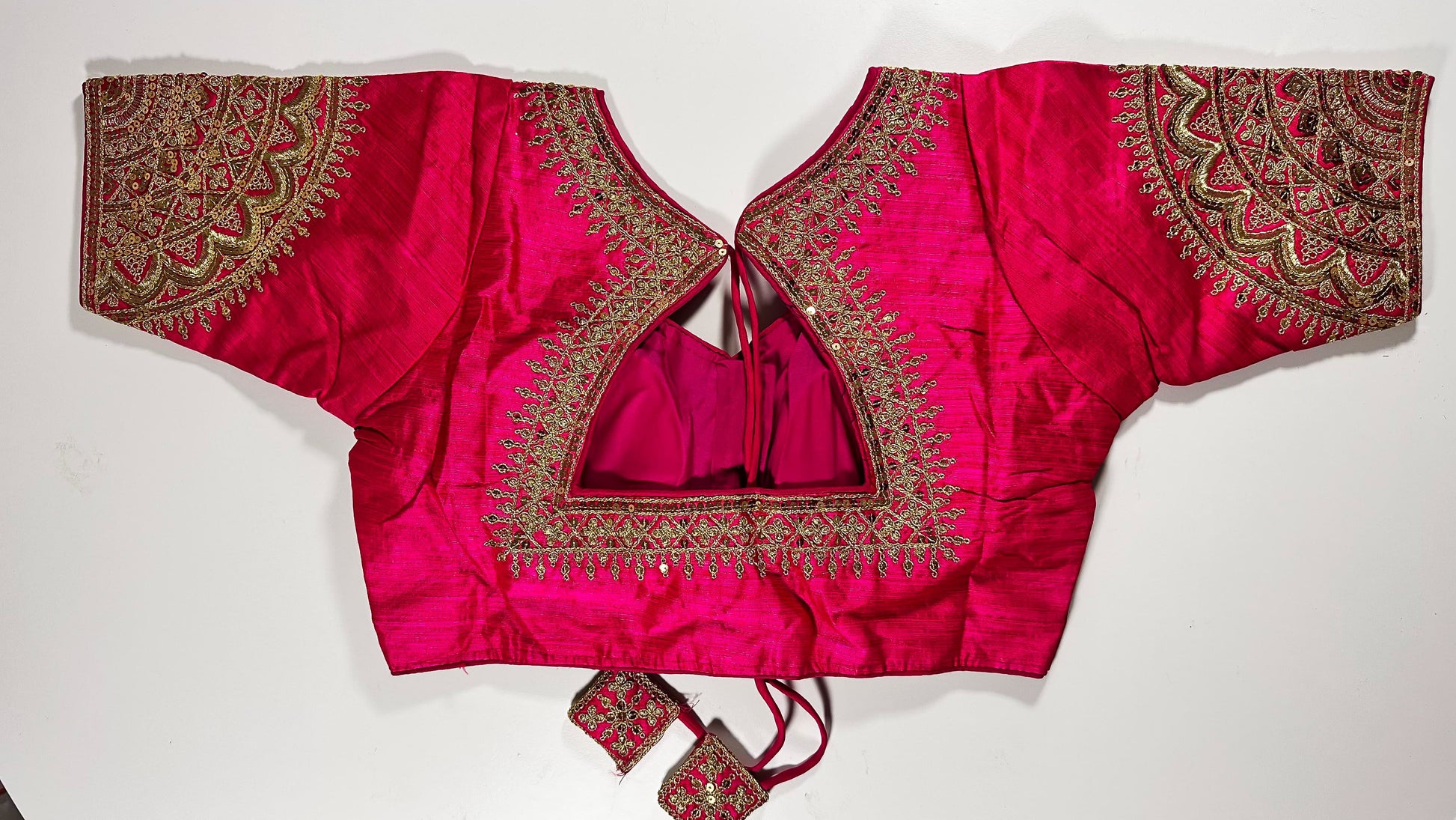 Back view of pink silk blouse showing tie-up design with embroidered tassels and detailed traditional embroidery work