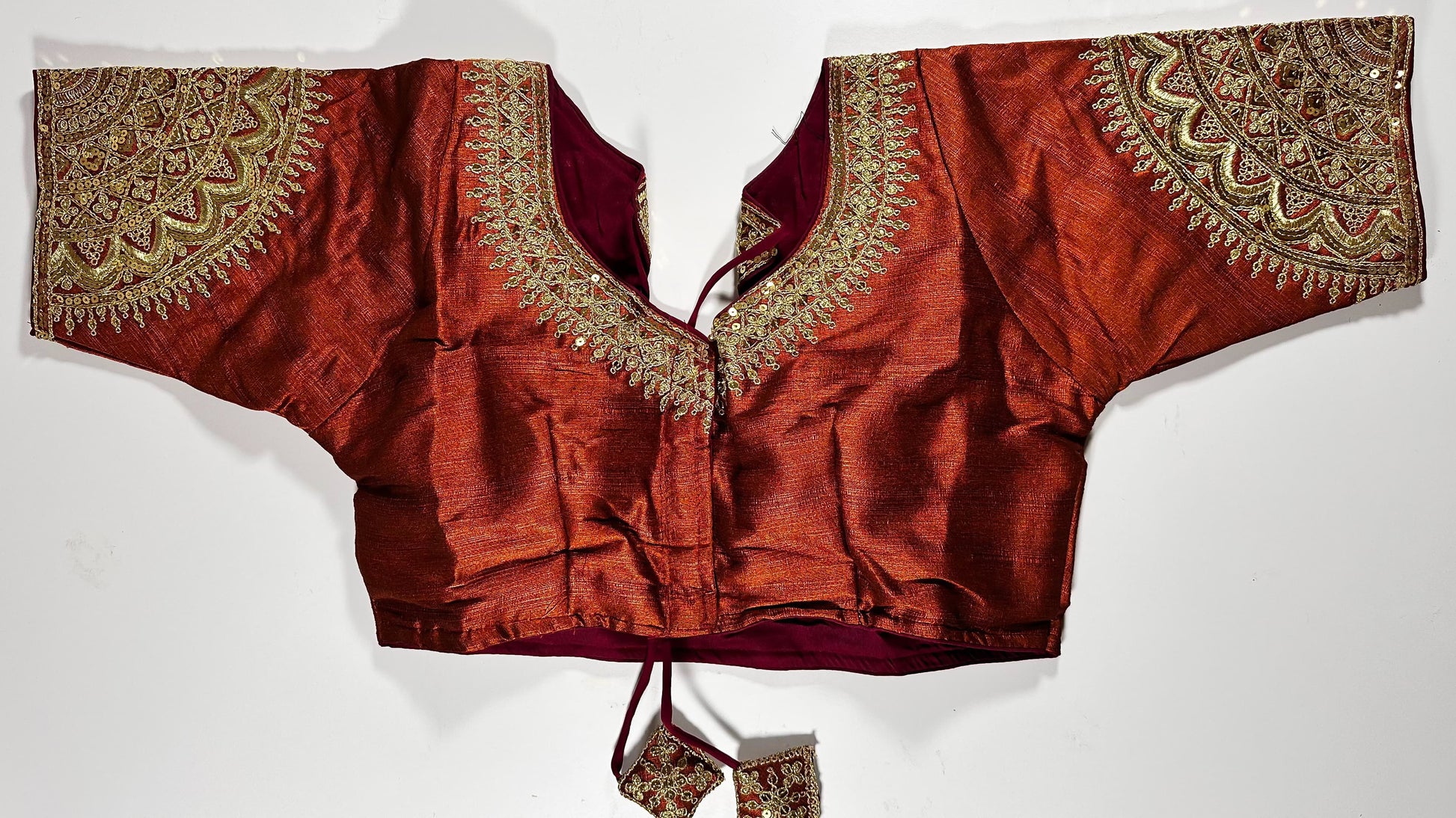 Rust red silk saree blouse with gold zardozi embroidery, featuring paisley motifs and traditional Indian threadwork - front view with decorative tassels