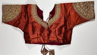 Rust red silk saree blouse with gold zardozi embroidery, featuring paisley motifs and traditional Indian threadwork - front view with decorative tassels