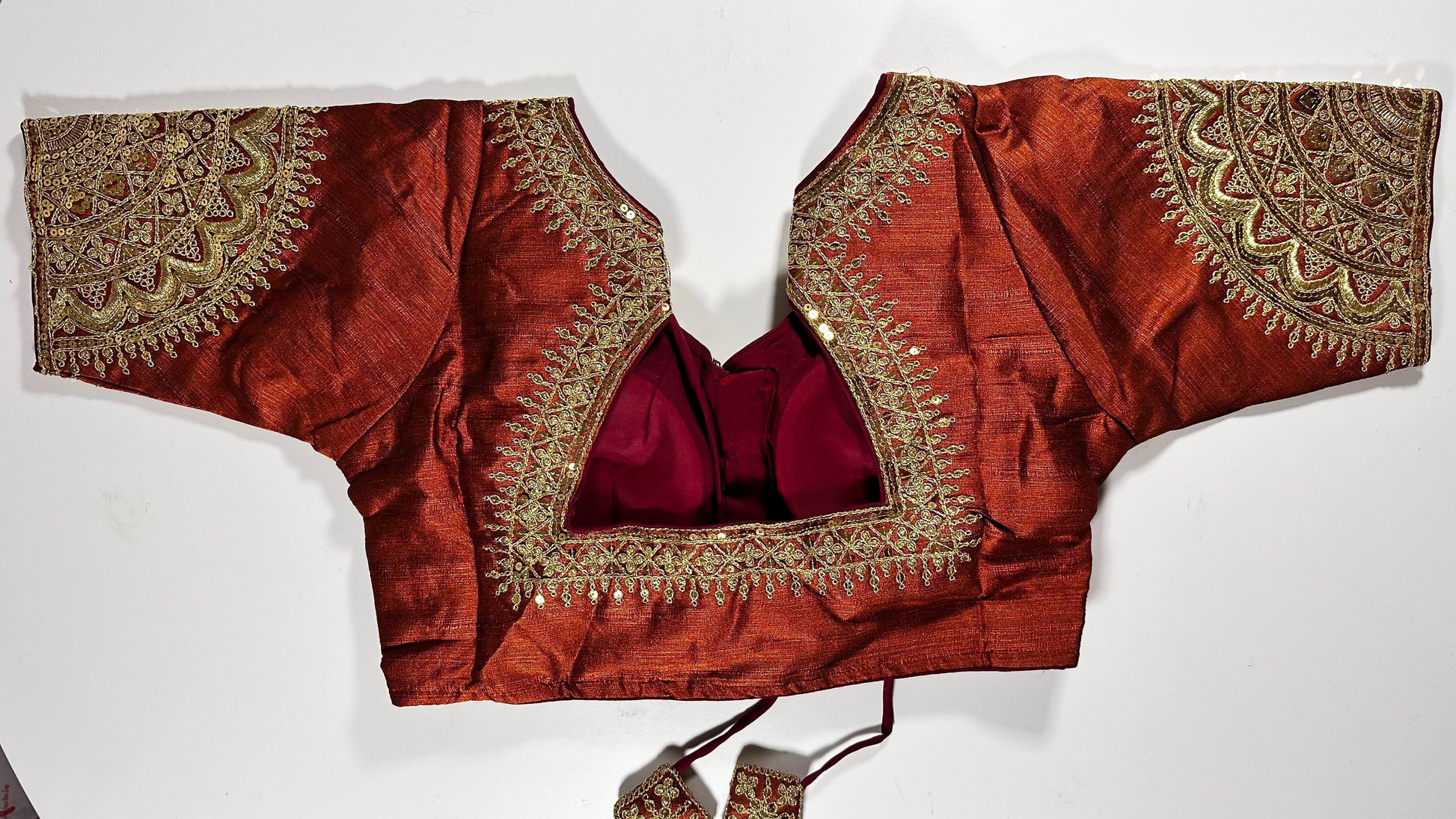 Back view of copper-red embroidered saree blouse showing detailed gold work, hook closure, and three-quarter sleeve design - Indian wedding wear UK