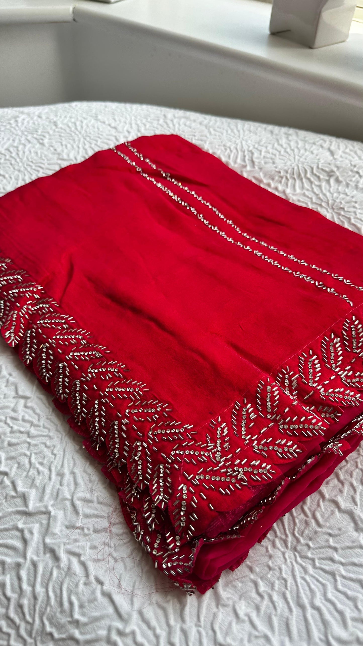 Luxurious barberry red saree with intricate golden hand embroidery featuring delicate leaf patterns, elegantly draped and displayed on white fabric background