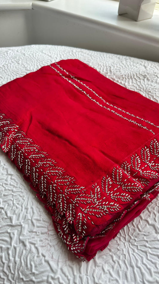 Luxurious barberry red saree with intricate golden hand embroidery featuring delicate leaf patterns, elegantly draped and displayed on white fabric background