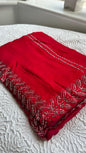 Luxurious barberry red saree with intricate golden hand embroidery featuring delicate leaf patterns, elegantly draped and displayed on white fabric background