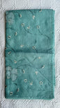 Beautiful sage green kota cotton saree with delicate white and green applique floral work scattered across the fabric, featuring decorative border trim, displayed on white textured background