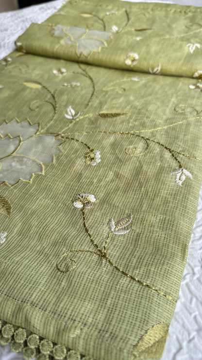 Beautiful olive green kota cotton saree with delicate lotus applique work and floral embroidery scattered across the fabric, featuring decorative scalloped border, displayed on white textured background