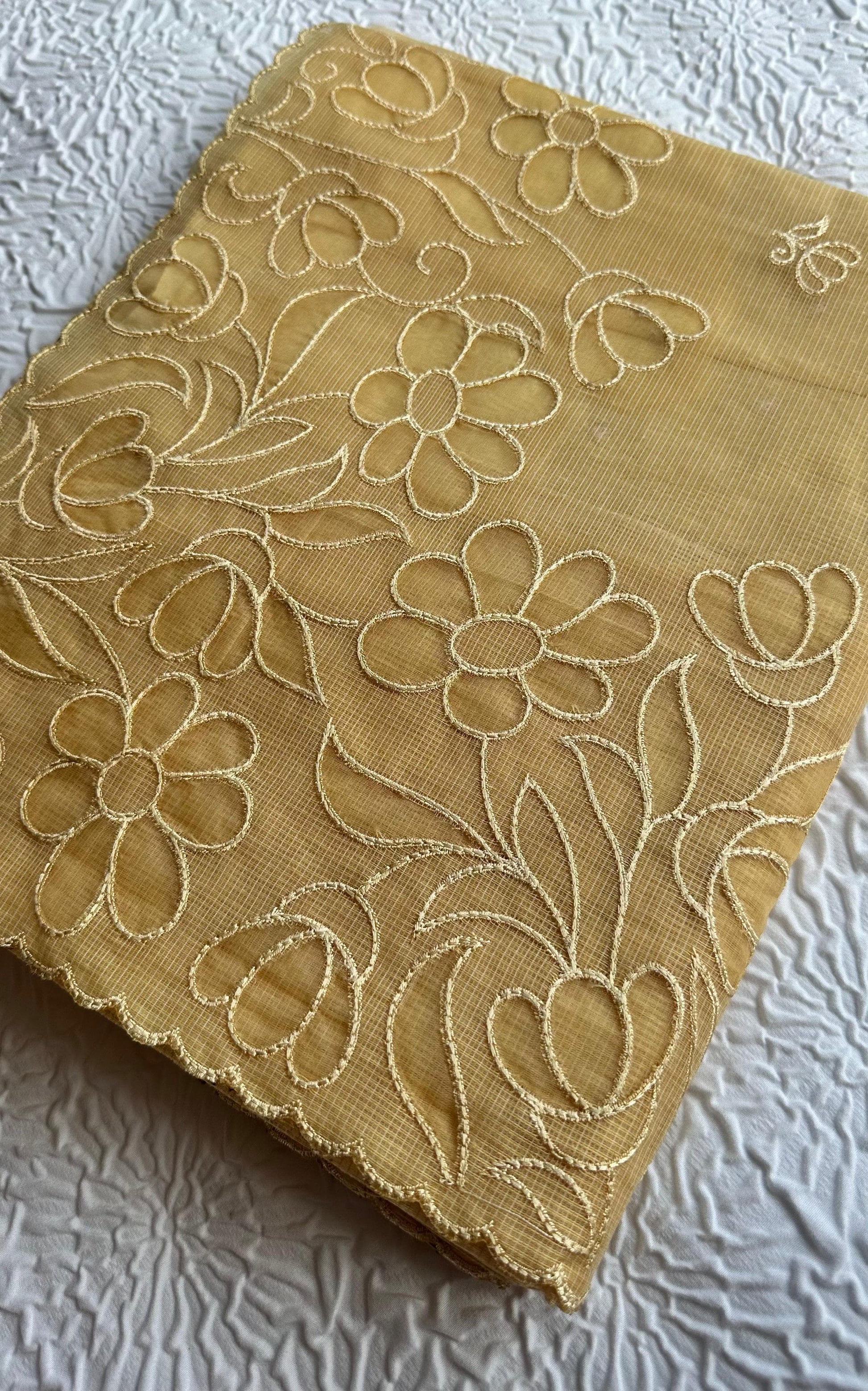 Radiant golden yellow kota cotton saree with beautiful floral applique work featuring delicate flower motifs and vine patterns with scalloped border detailing, elegantly displayed on white textured background