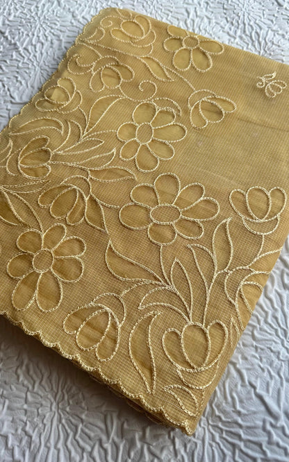 Radiant golden yellow kota cotton saree with beautiful floral applique work featuring delicate flower motifs and vine patterns with scalloped border detailing, elegantly displayed on white textured background