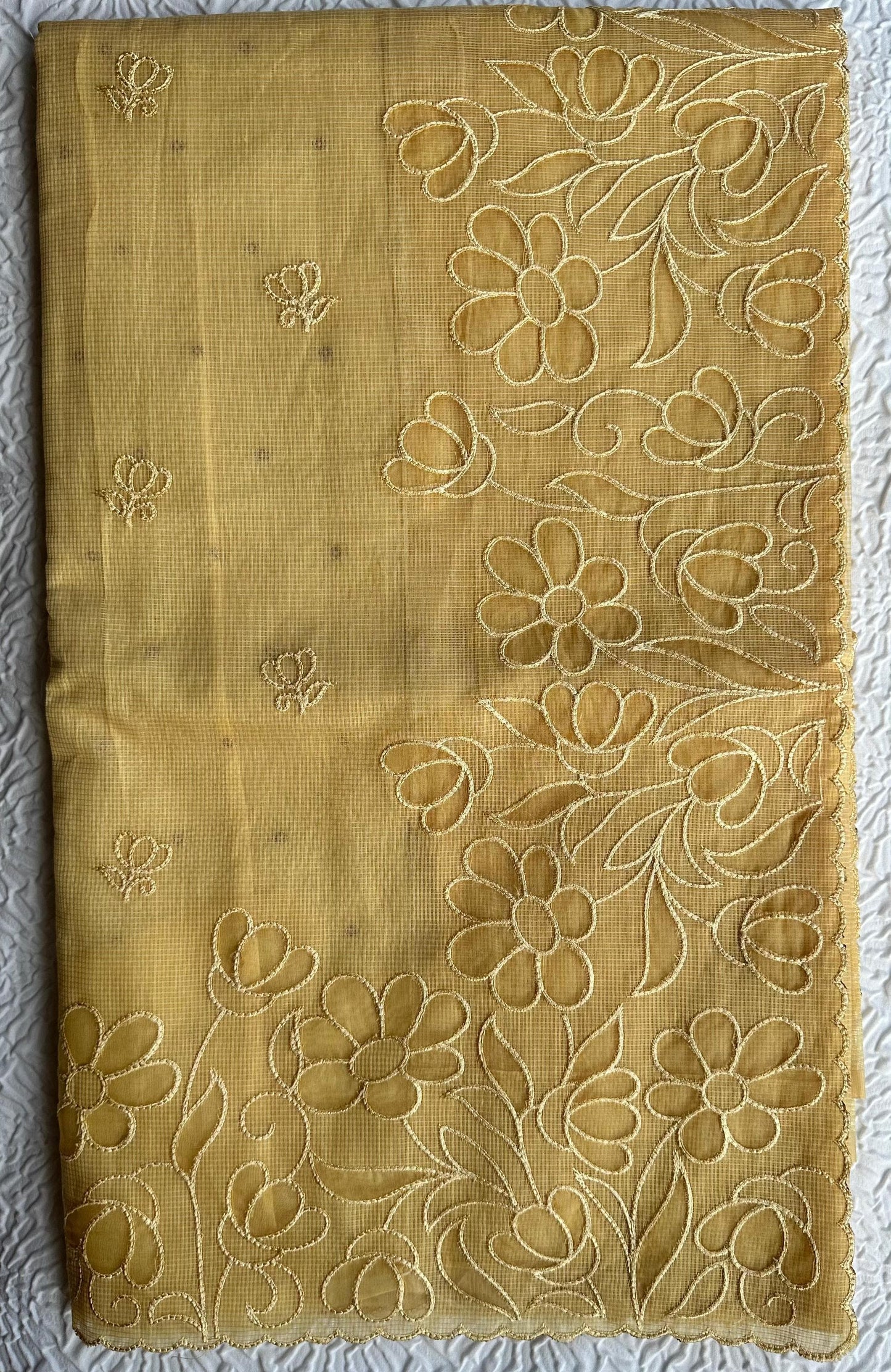 Radiant golden yellow kota cotton saree with beautiful floral applique work featuring delicate flower motifs and vine patterns with scalloped border detailing, elegantly displayed on white textured background