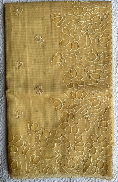 Radiant golden yellow kota cotton saree with beautiful floral applique work featuring delicate flower motifs and vine patterns with scalloped border detailing, elegantly displayed on white textured background