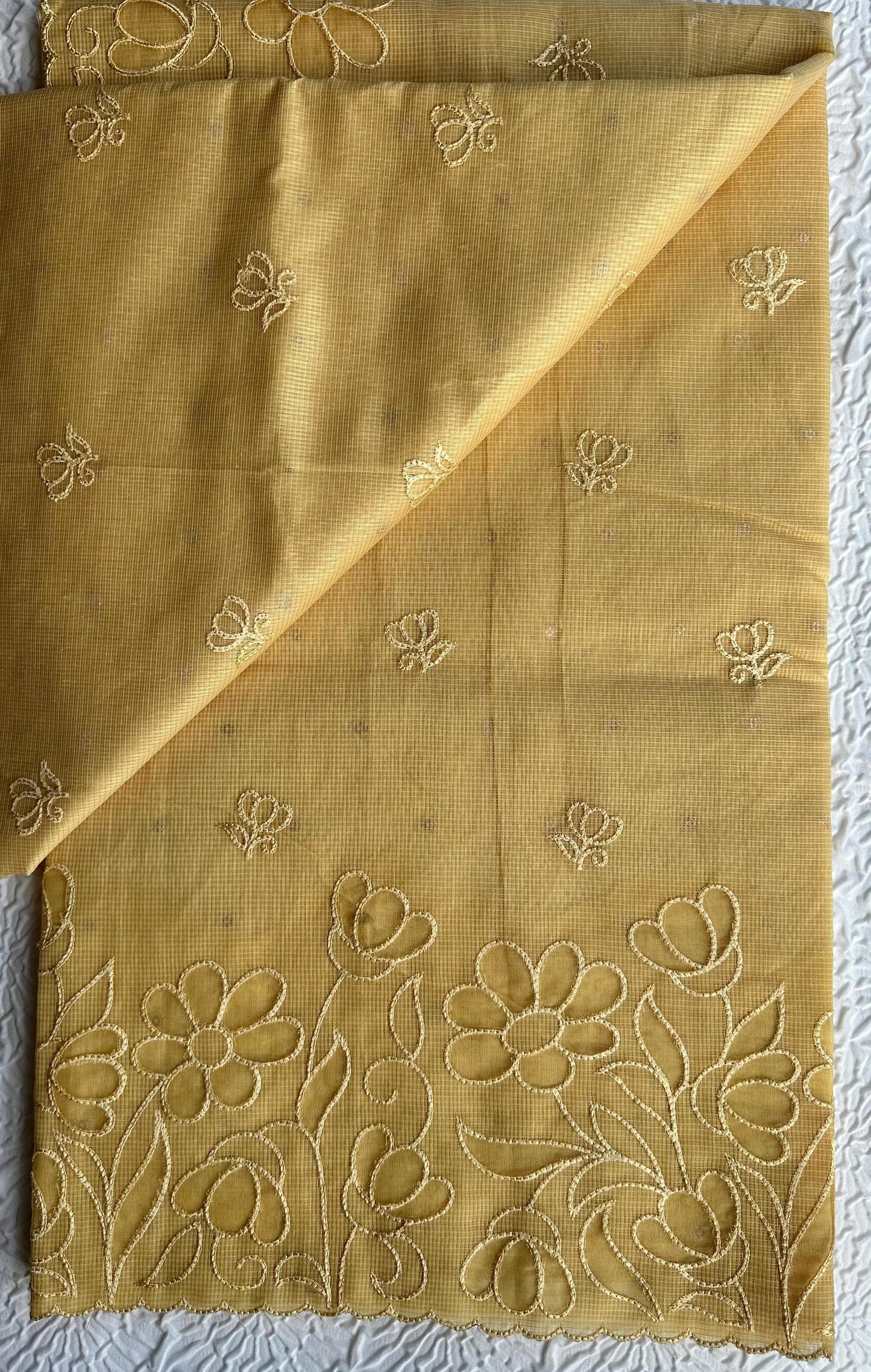 Radiant golden yellow kota cotton saree with beautiful floral applique work featuring delicate flower motifs and vine patterns with scalloped border detailing, elegantly displayed on white textured background