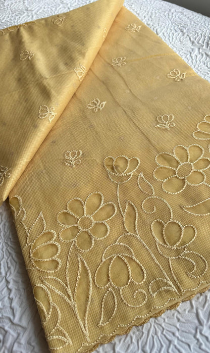 Radiant golden yellow kota cotton saree with beautiful floral applique work featuring delicate flower motifs and vine patterns with scalloped border detailing, elegantly displayed on white textured background