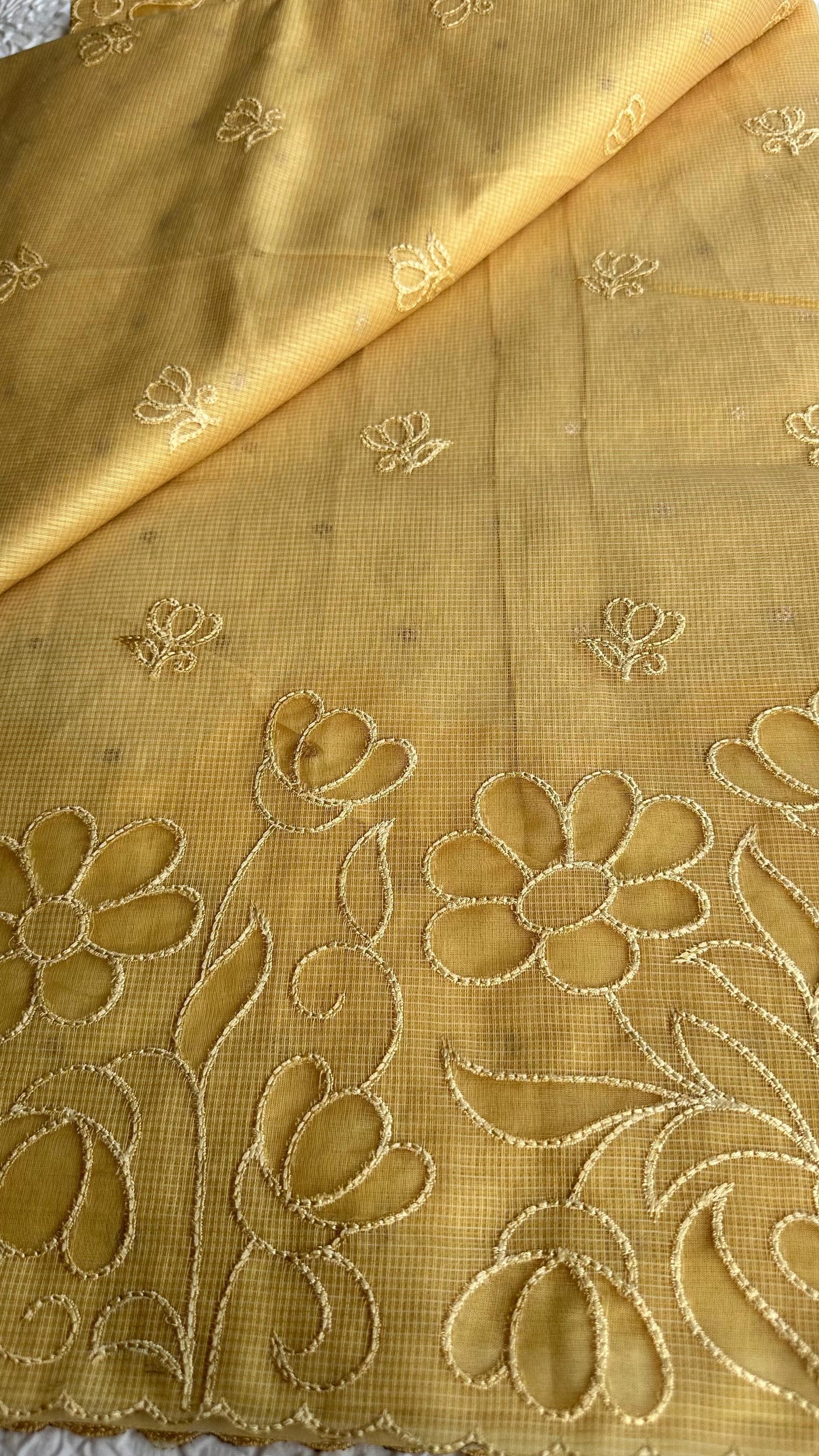 Radiant golden yellow kota cotton saree with beautiful floral applique work featuring delicate flower motifs and vine patterns with scalloped border detailing, elegantly displayed on white textured background