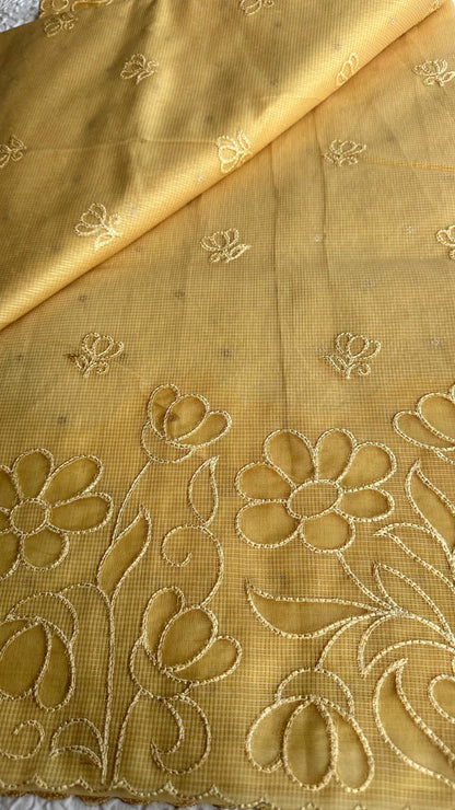 Radiant golden yellow kota cotton saree with beautiful floral applique work featuring delicate flower motifs and vine patterns with scalloped border detailing, elegantly displayed on white textured background