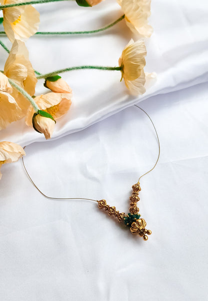 Golden bead and emerald cluster necklace with intricate design, displayed on a white background with floral decoration.