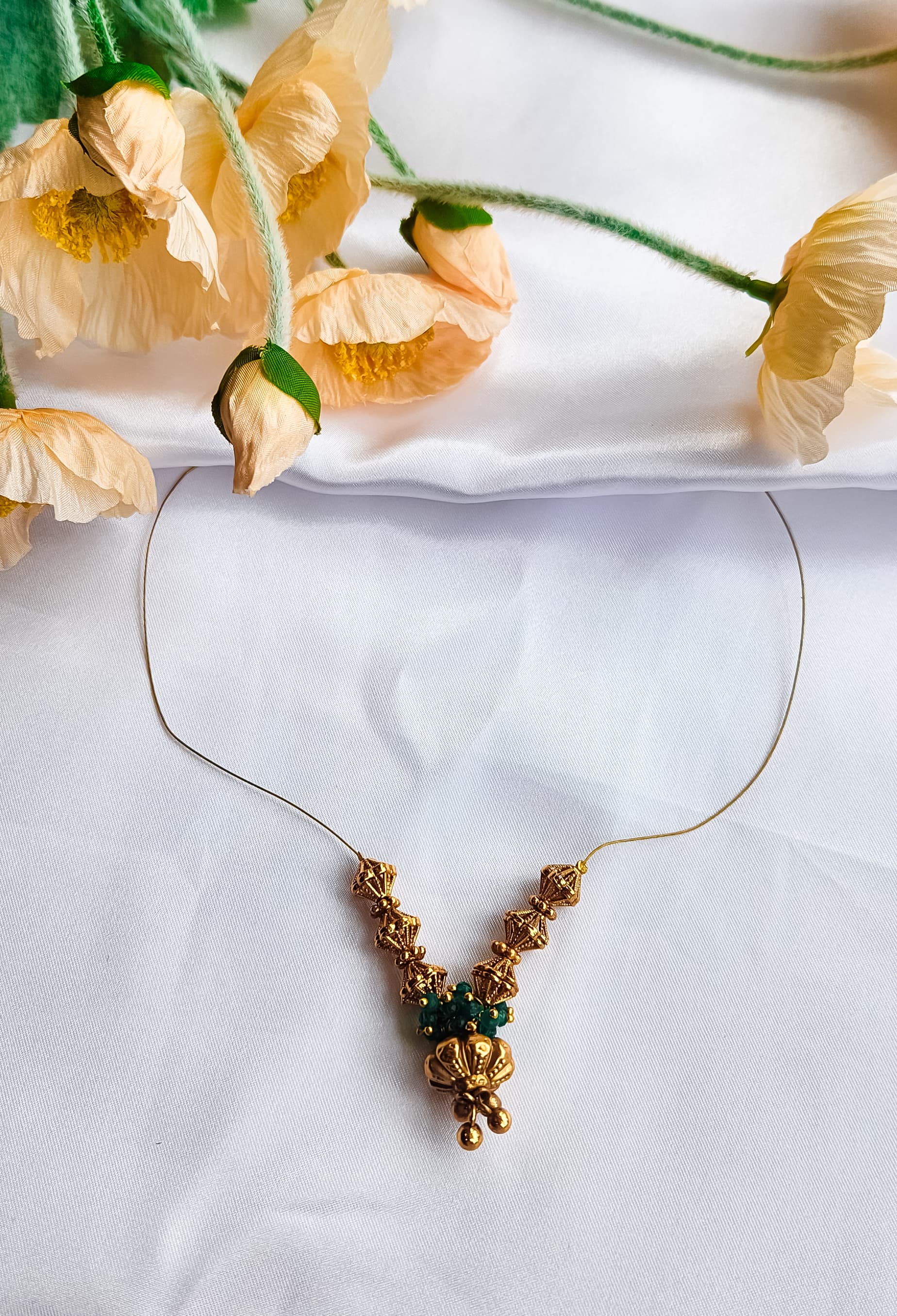 Golden bead and emerald cluster necklace with intricate design, displayed on a white background with floral decoration.