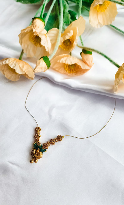 Golden bead and emerald cluster necklace with intricate design, displayed on a white background with floral decoration.