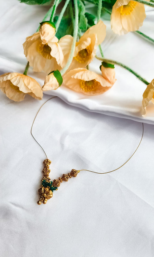 Golden bead and emerald cluster necklace with intricate design, displayed on a white background with floral decoration.
