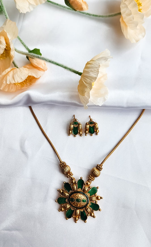 Traditional green and gold sunburst necklace set with matching earrings displayed on white silk cloth with flowers.
