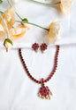 Traditional red stone necklace set with floral pendant, pearl drop accents, and matching red stone earrings displayed on white fabric with flowers.