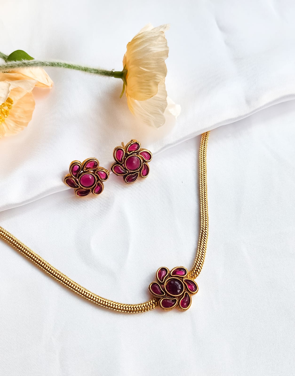 Pink Floral Bloom Necklace Set featuring enamel flower motif and earrings, styled elegantly against white fabric and flowers.