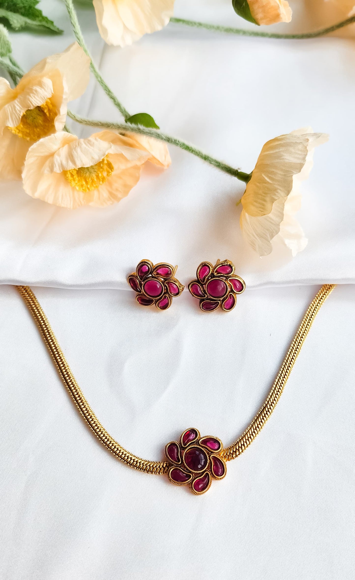 Pink Floral Bloom Necklace Set featuring enamel flower motif and earrings, styled elegantly against white fabric and flowers.