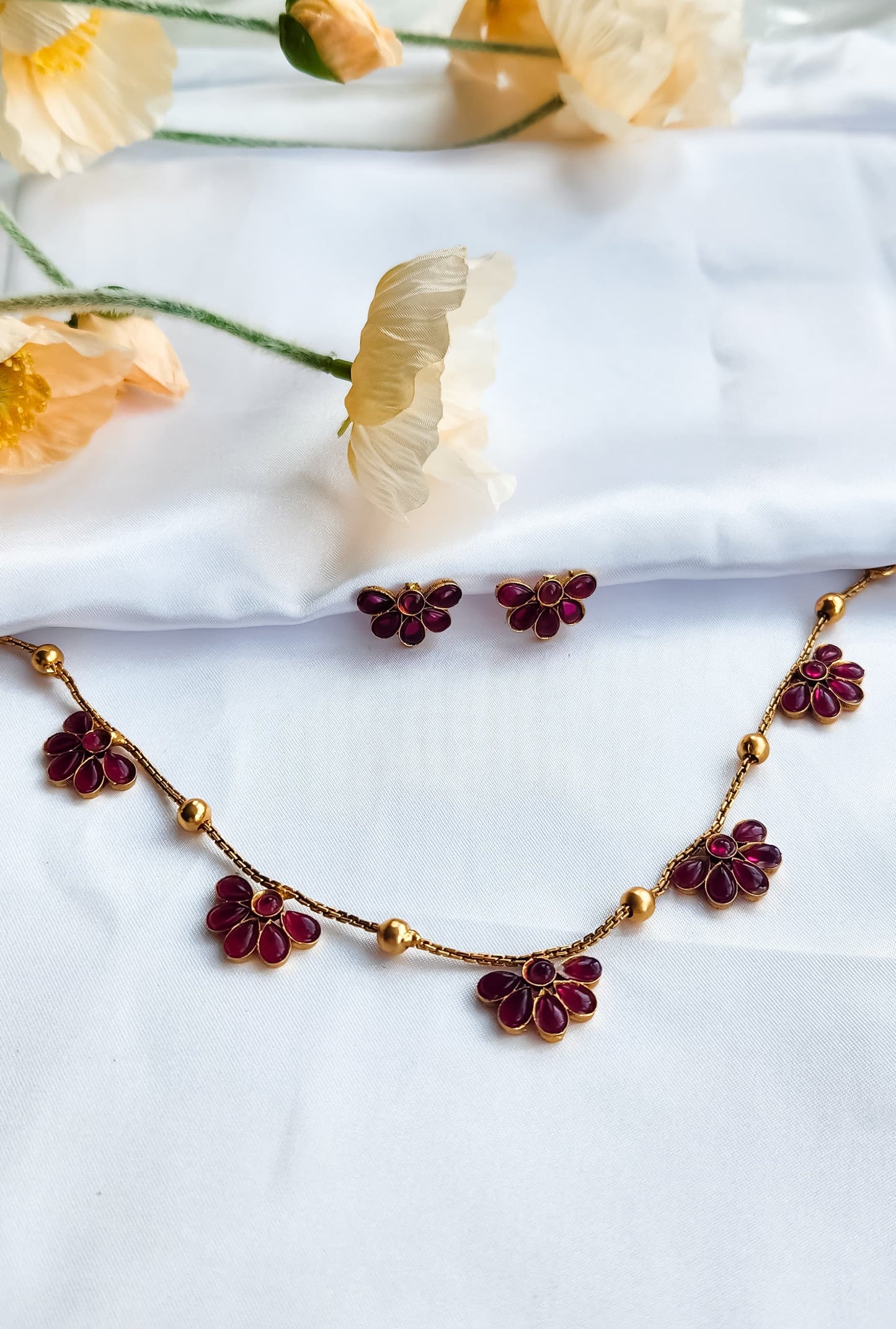 Elegant pink floral necklace and earrings set with gold detailing, displayed on white cloth.