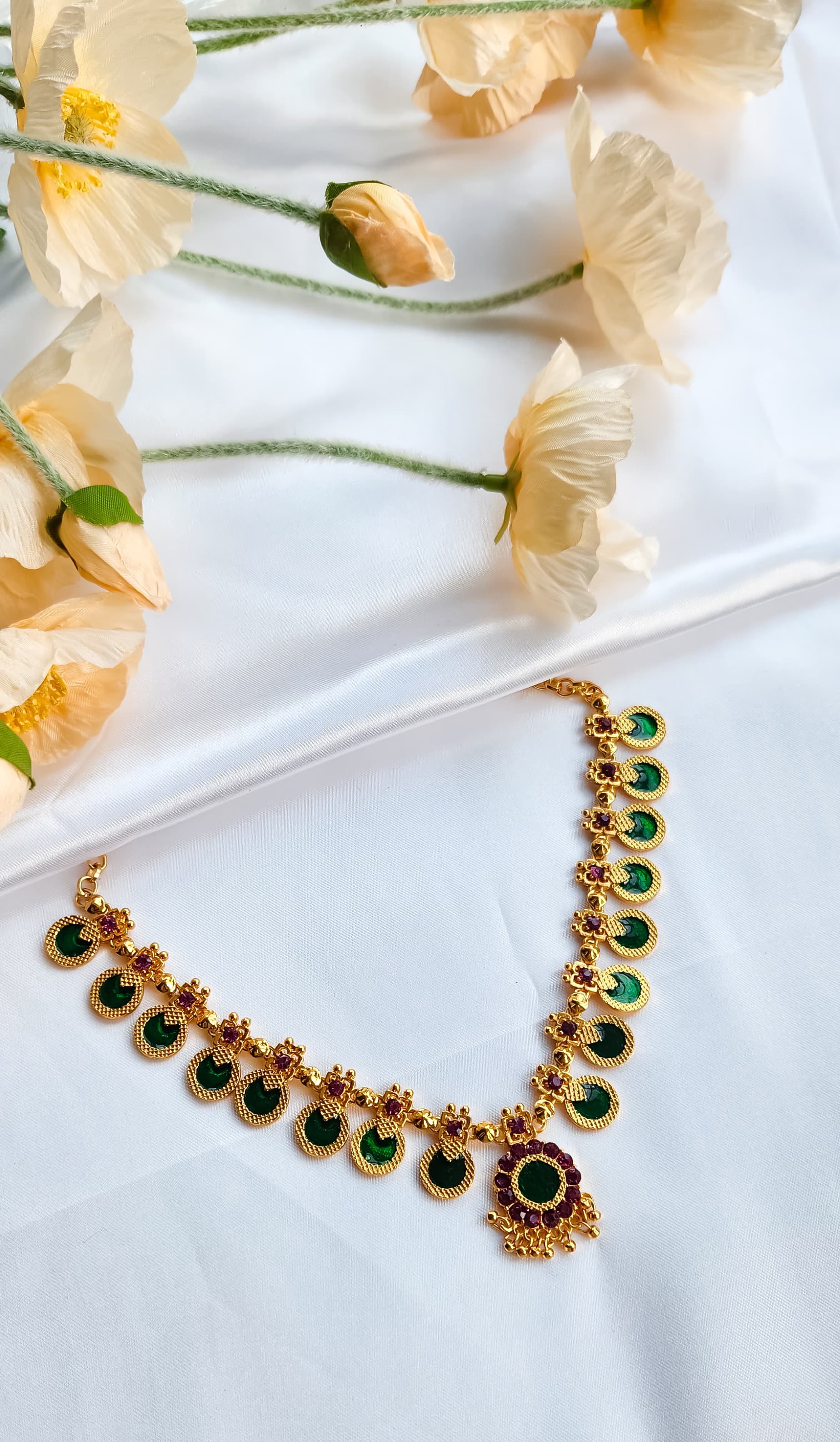 Elegant kasu choker necklace with central floral pendant, displayed on white silk cloth with peach flowers.