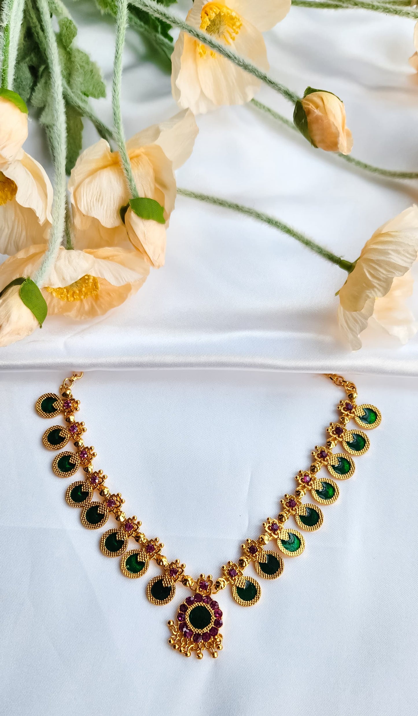 Close-up of antique gold choker necklace featuring alternating green kasu and ruby stone floral details.