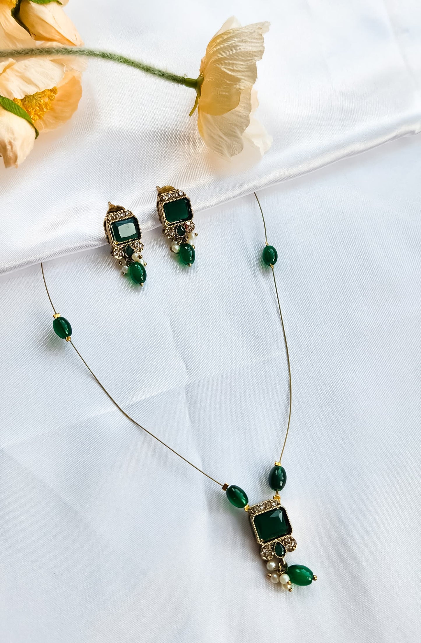 Gold-toned kundan-style necklace with green square stone pendant, matching earrings, and pearl accents