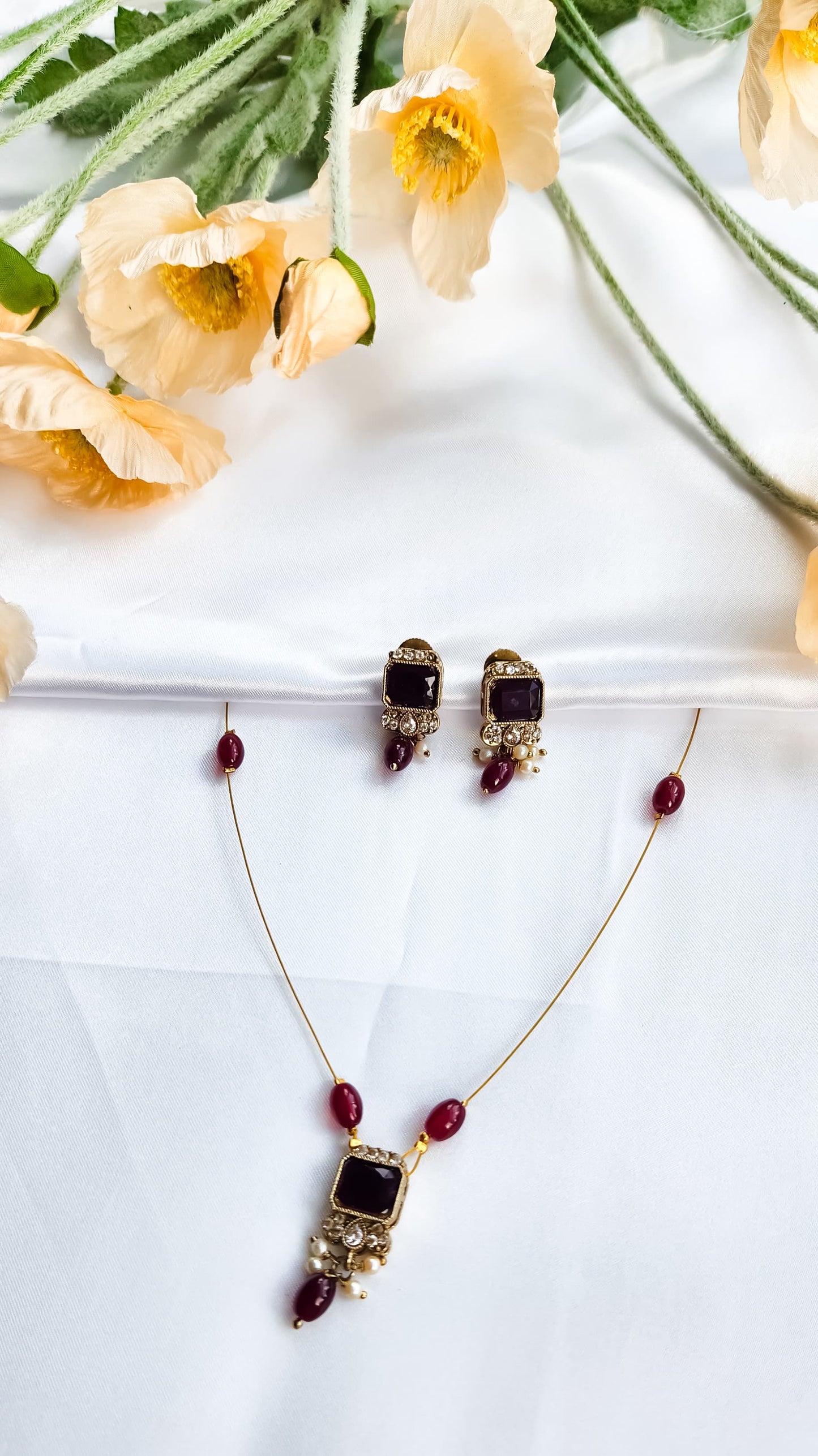 Gold-toned kundan-style necklace with red square stone pendant, matching earrings, and pearl accents