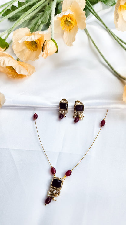 Gold-toned kundan-style necklace with red square stone pendant, matching earrings, and pearl accents