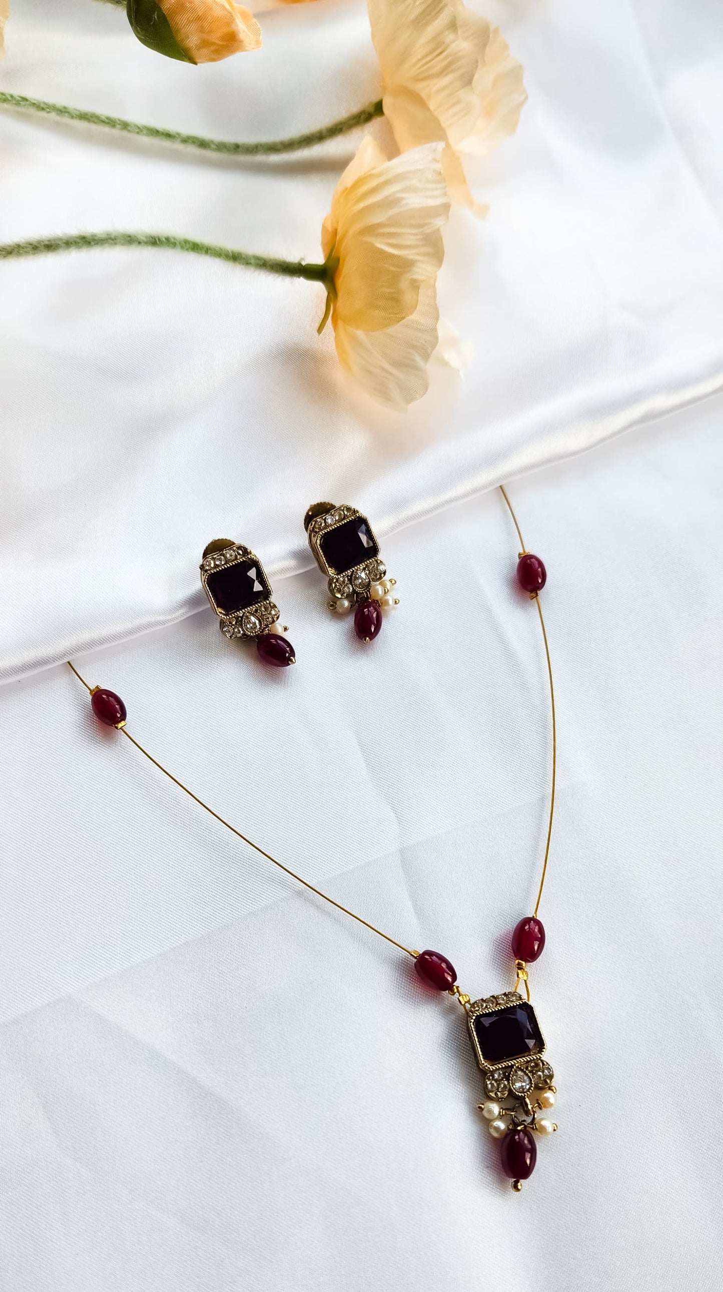 Gold-toned kundan-style necklace with red square stone pendant, matching earrings, and pearl accents