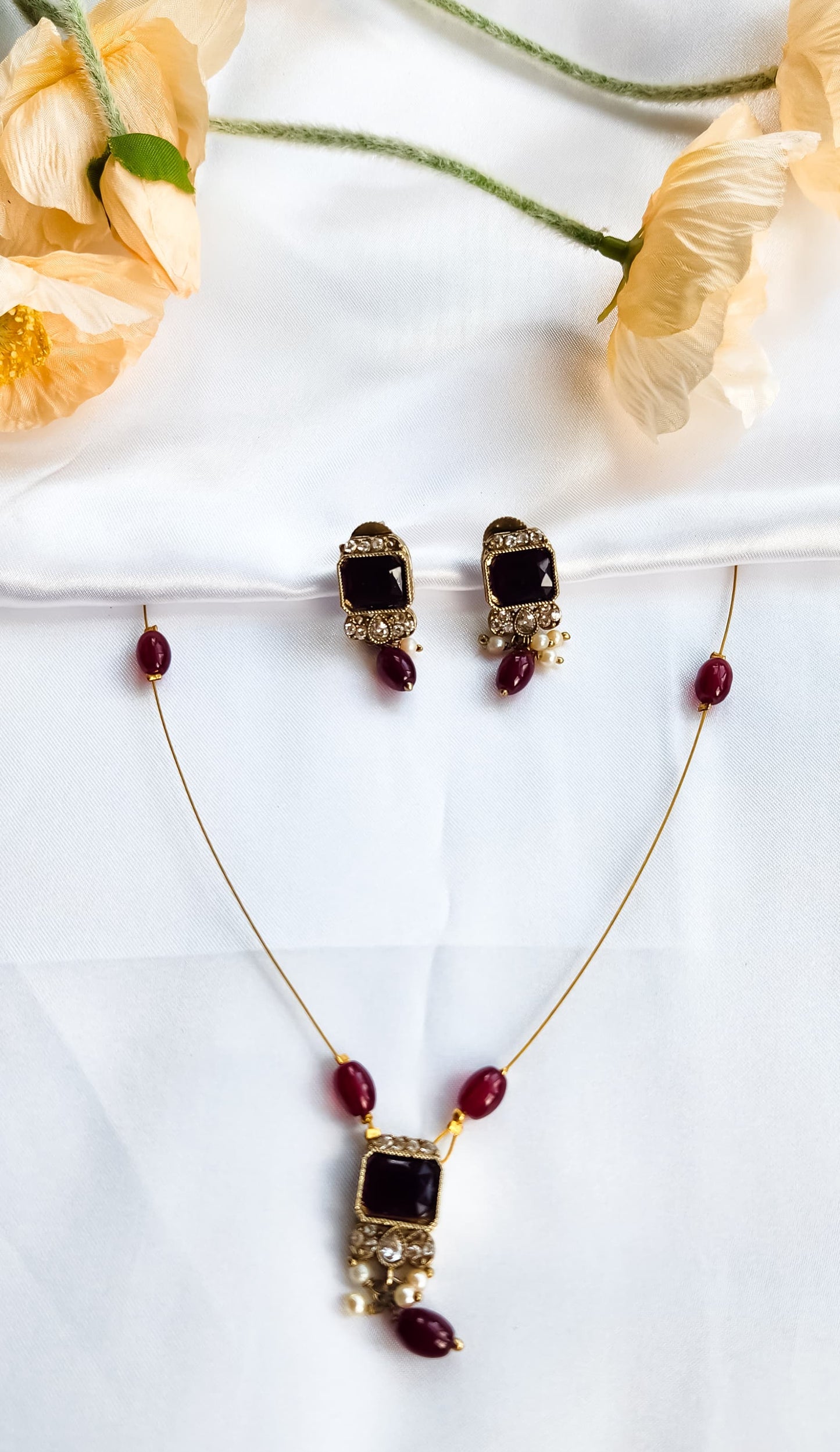 Gold-toned kundan-style necklace with red square stone pendant, matching earrings, and pearl accents
