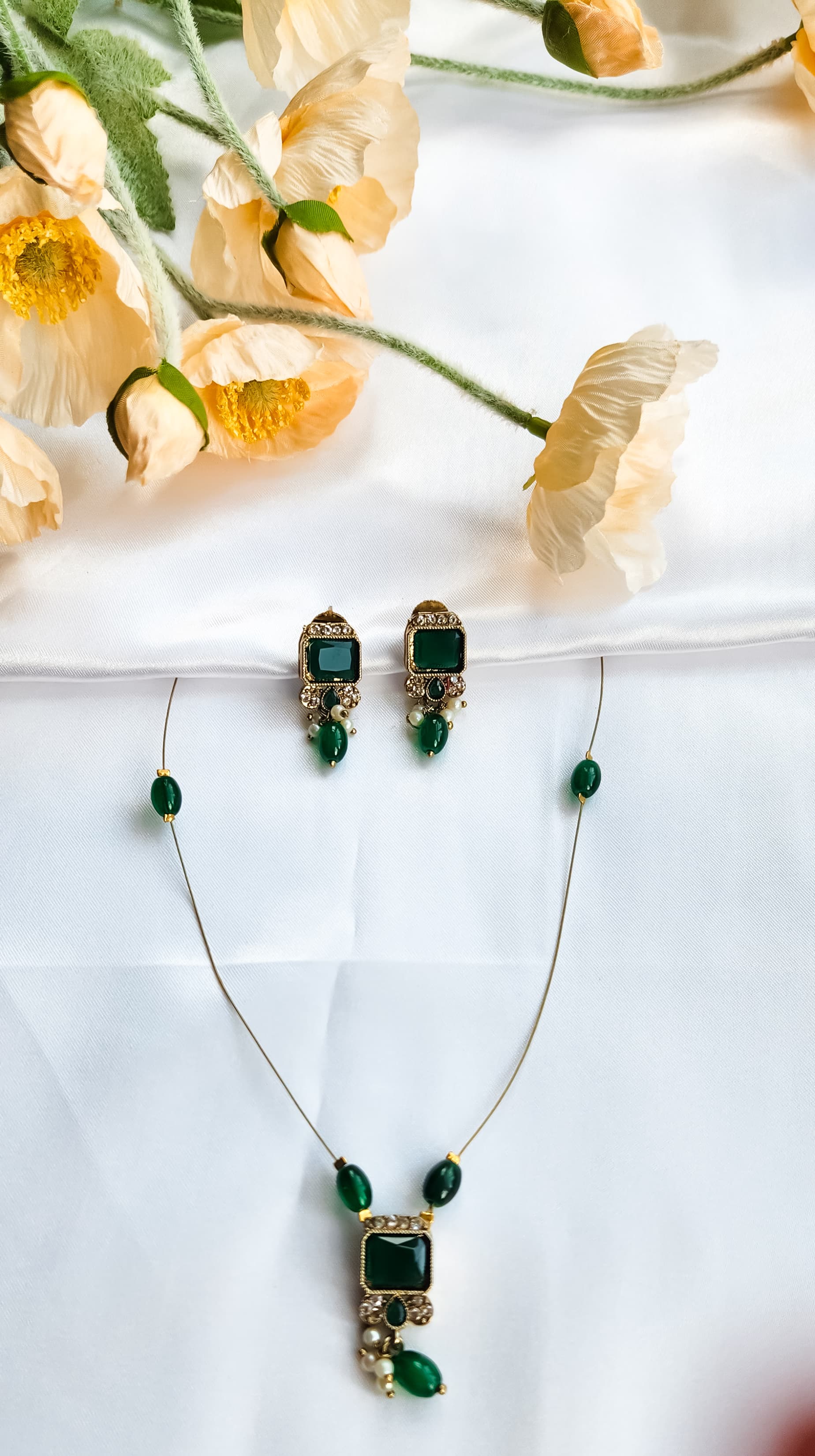 Gold-toned kundan-style necklace with green square stone pendant, matching earrings, and pearl accents