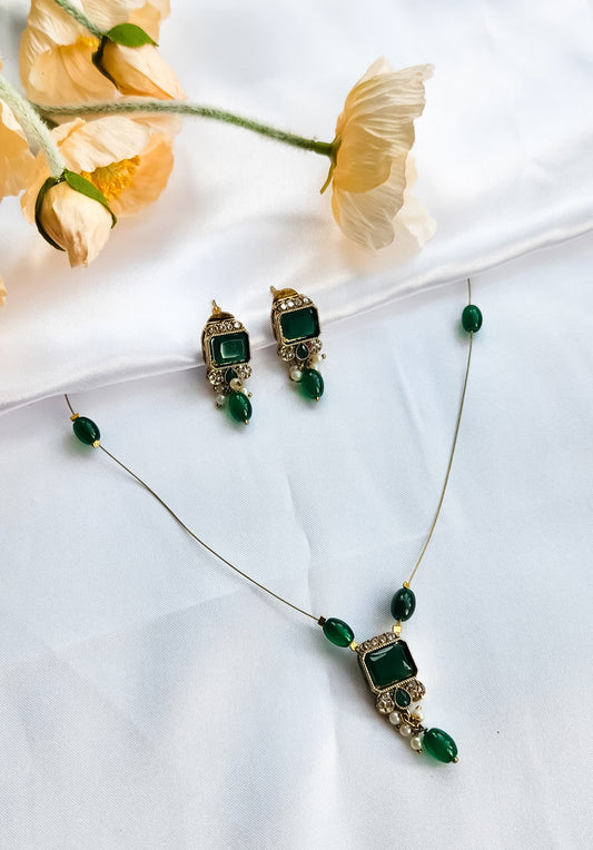 Gold-toned kundan-style necklace with green square stone pendant, matching earrings, and pearl accents
