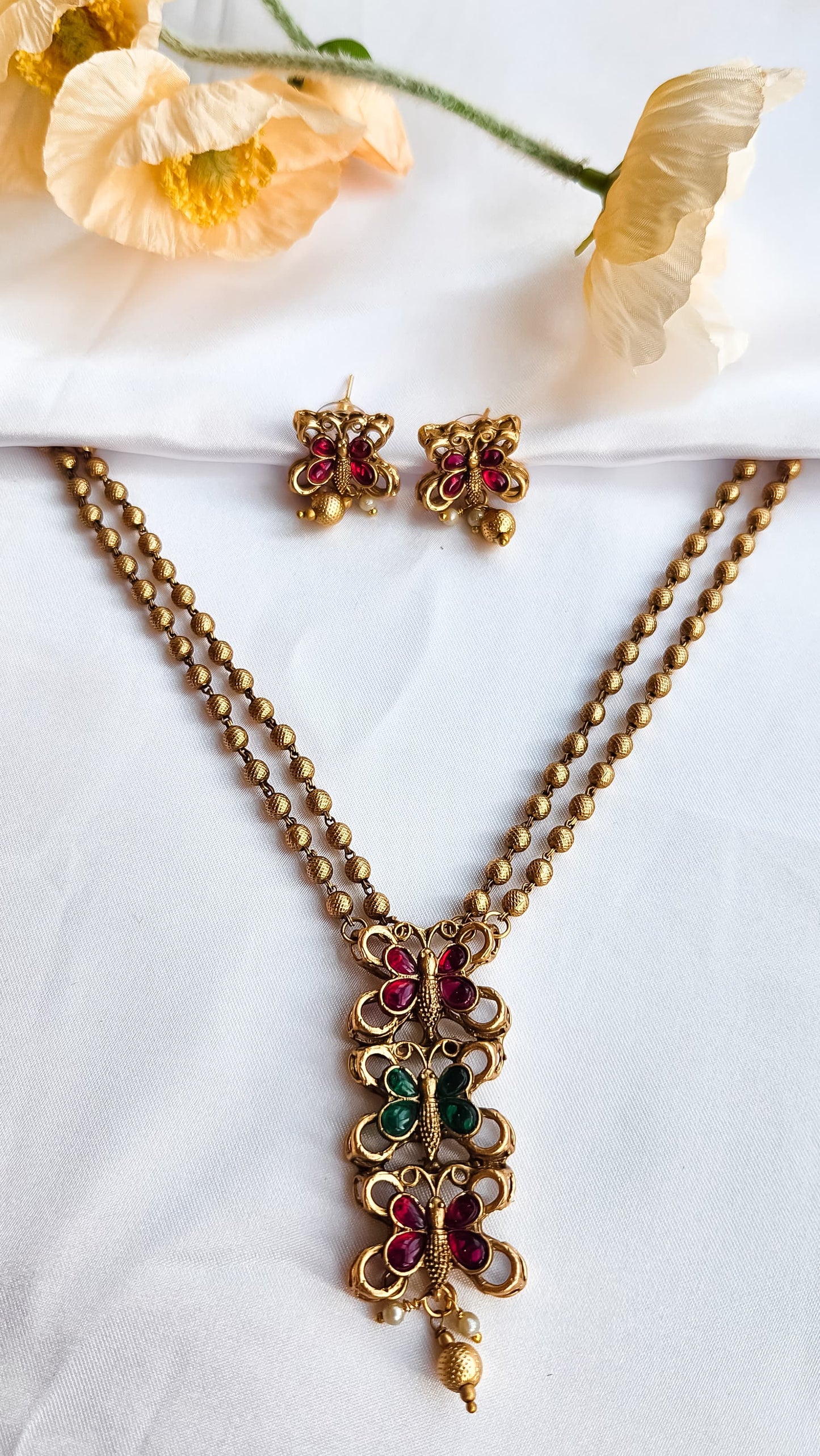 Gold finish butterfly design necklace with ruby and green stones, paired with matching butterfly earrings, golden bead chain.