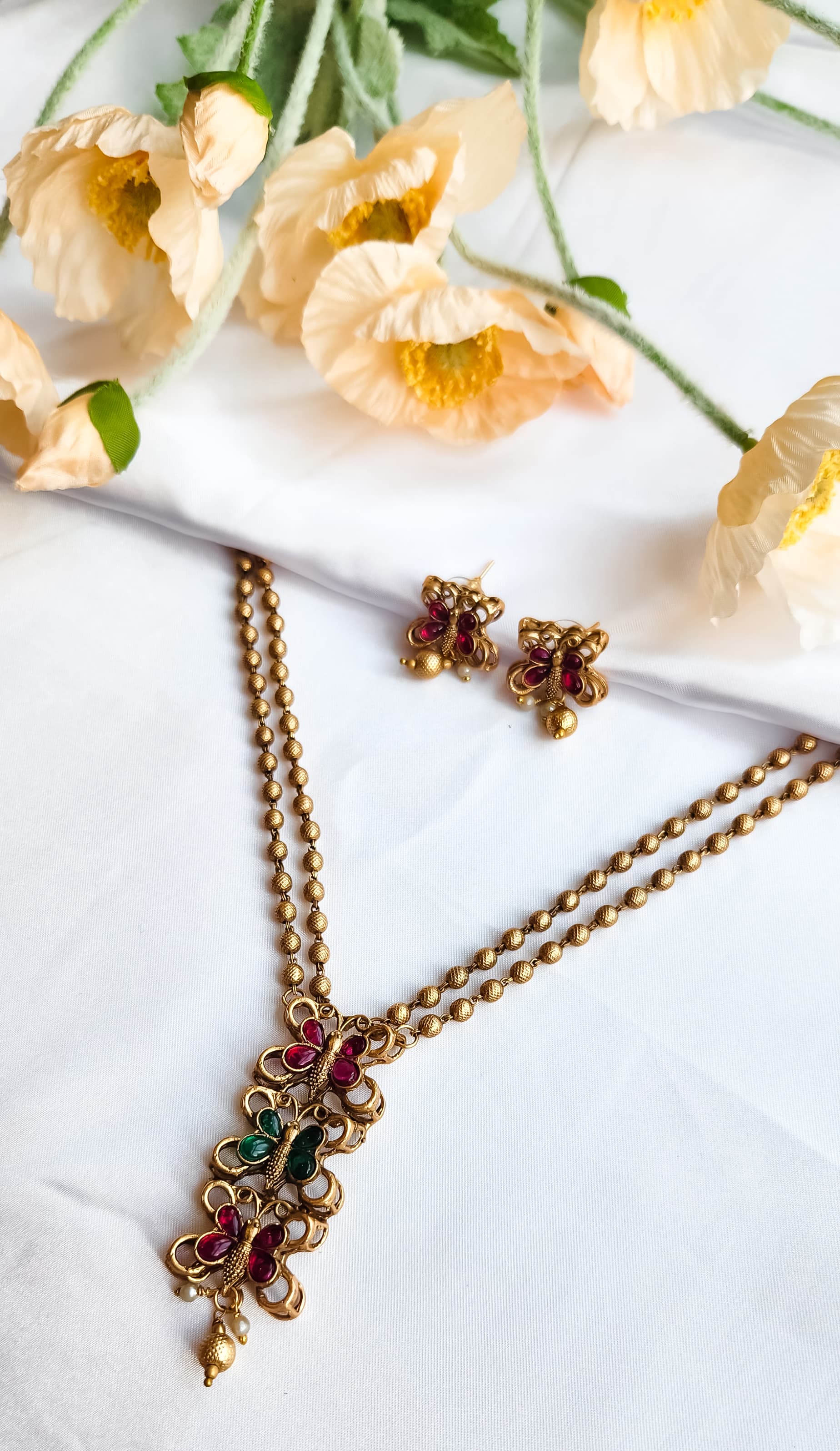 Gold finish butterfly design necklace with ruby and green stones, paired with matching butterfly earrings, golden bead chain.