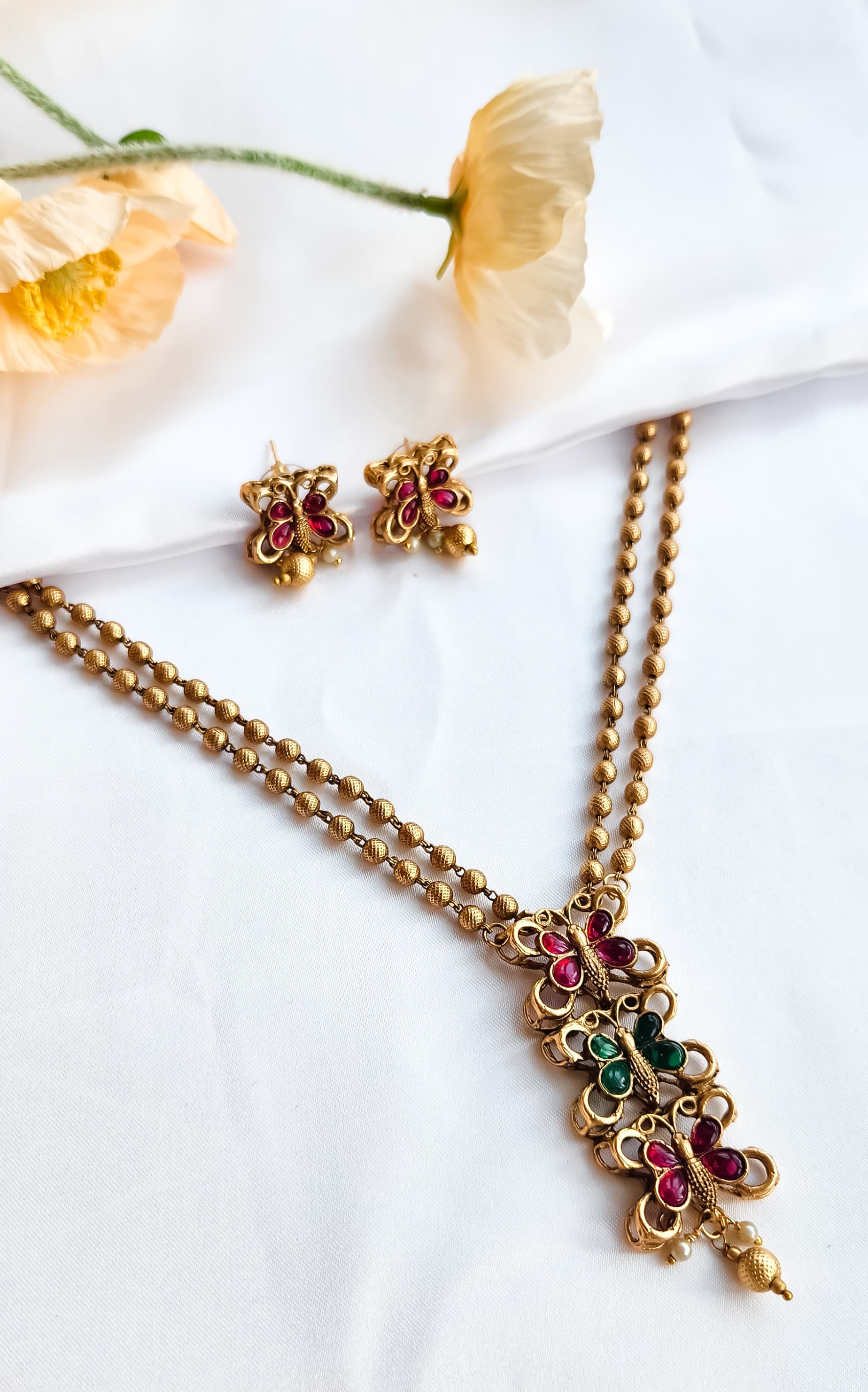 Gold finish butterfly design necklace with ruby and green stones, paired with matching butterfly earrings, golden bead chain.