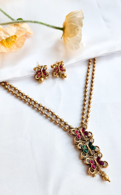 Gold finish butterfly design necklace with ruby and green stones, paired with matching butterfly earrings, golden bead chain.