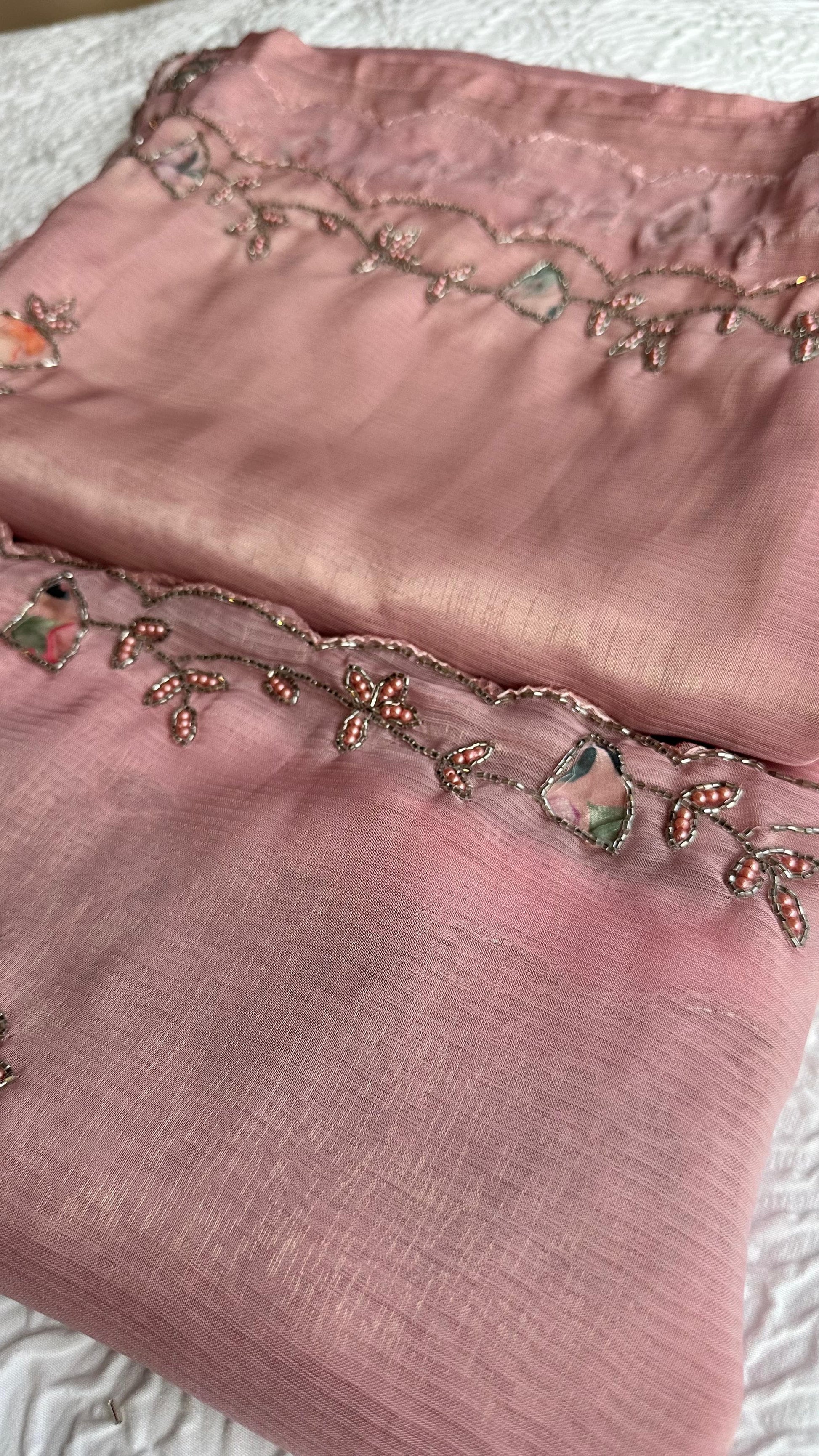 Close-up of pink saree fabric with floral bead embroidery and crystal-style accents.