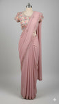 Pastel pink embroidered saree with floral bead border laid flat on white quilted surface.